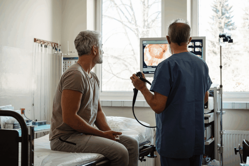 Médico observando as imagens do intestino no monitor ao lado de paciente sentado na maca