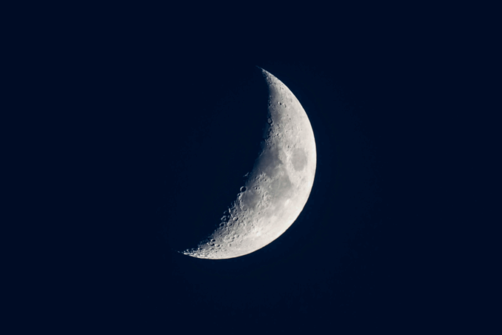 A imagem mostra a Lua em sua fase minguante, destacada contra um céu escuro e sem nuvens. Apenas parte de sua superfície está iluminada, enquanto o restante permanece na sombra, formando um semicírculo bem definido
