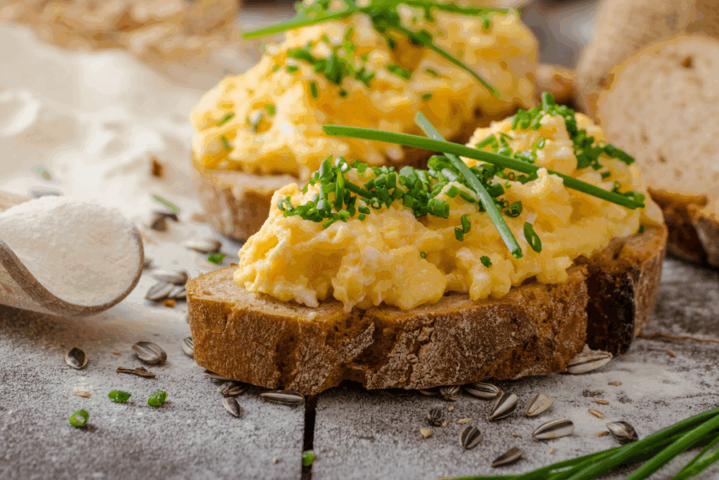 Dois pedaços de pães com patê de ovo e cebolinha picada em cima de uma mesa de madeira