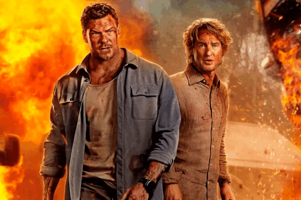 Imagem de “Três Horas Para Viver” com Alan Ritchson: dois homens com roupas sujas e rostos machucados caminham lado a lado em direção à câmera, com explosões e fogo ao fundo.